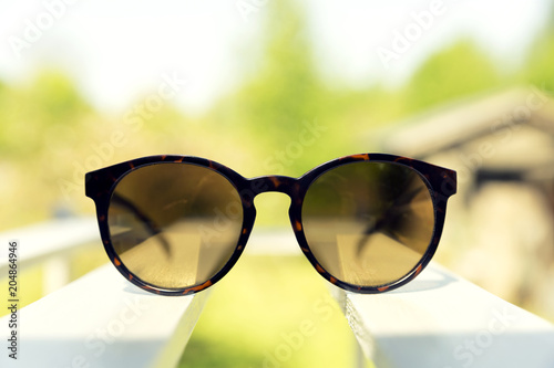 Sunglasses on white wooden bench, backyard in the background. Summer and fashion