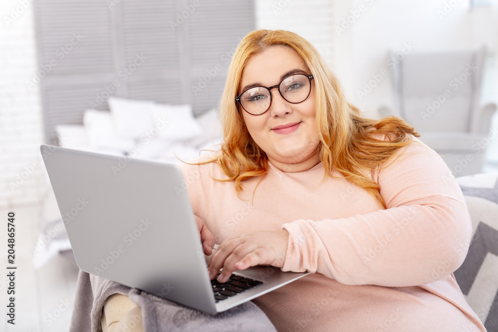 Good mood. Cheerful overweight woman wearing glasses and working on her laptop Good mood. Cheerful overweight woman wearing glasses and working on her laptop