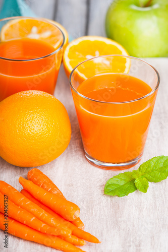Glasses with carrot juice, apple, mint leaf and sliced orange 