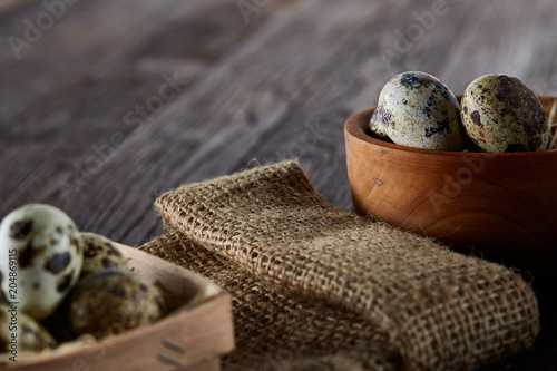 Fototapeta Naklejka Na Ścianę i Meble -  Rustic still life with quail eggs in bucket, box and bowl on a linen napkin over wooden background, selective focus
