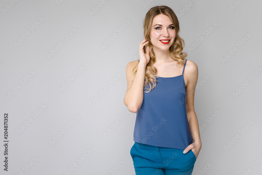 Charming girl with white long curly hair. Girl in a blue top and blue pants on gray background Charming girl with white long curly hair. Girl in a blue top and blue pants on gray background