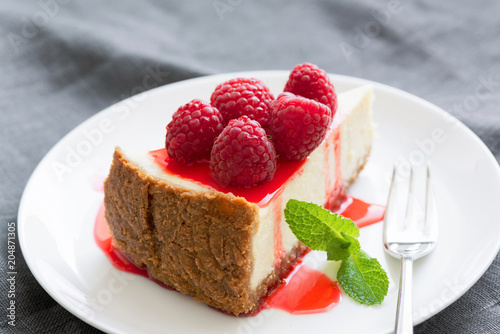 Cheesecake with berry sauce and fresh raspberries on white plate. Selective focus  horizontal composition