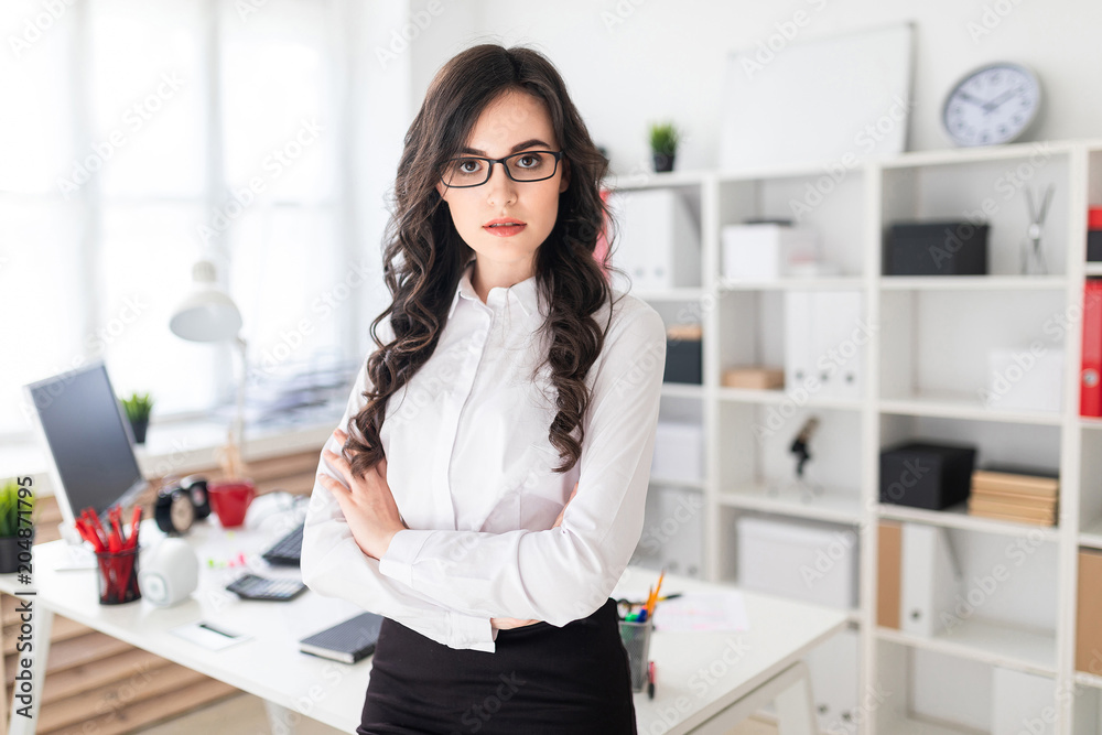 A beautiful young girl stands near the office table, hands clasped on her chest.