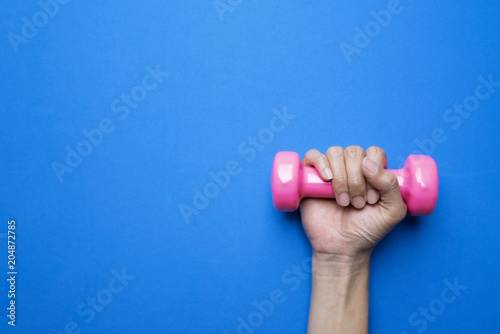 woman hand holding pink dumbbell on blue background, sport and healthy lifestyle concept