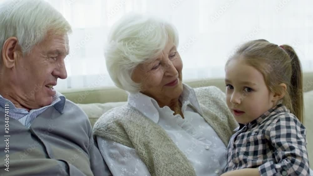 Medium shot of cheerful grandmother and grandfather chatting with cute preschool girl while babysitting Medium shot of cheerful grandmother and grandfather chatting with cute preschool girl while babysitting