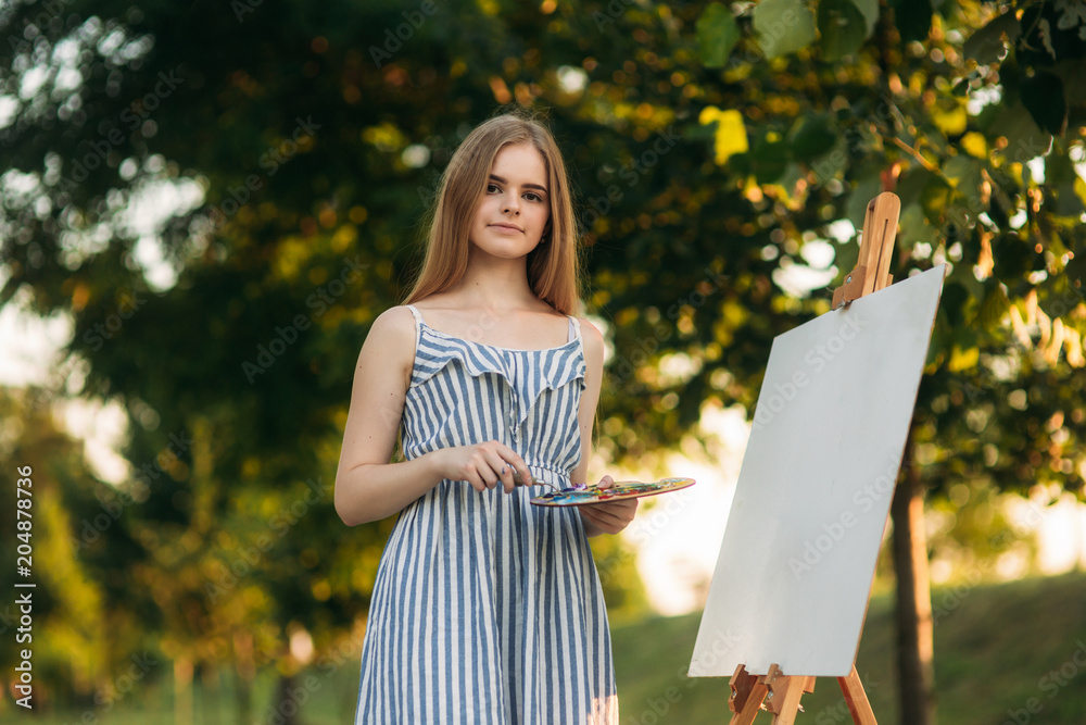 Naklejka premium Beautiful girl artist is standing in the park and holding palette with paints