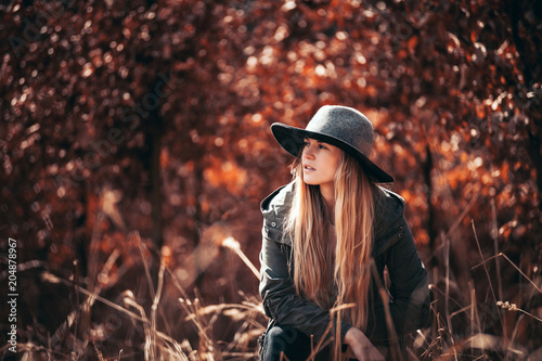 Stylish girl with long hair and hat walking in golden autumn forest