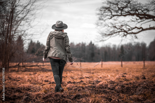 Rural scene with woman in hat walking on field, melancholic autumn mood