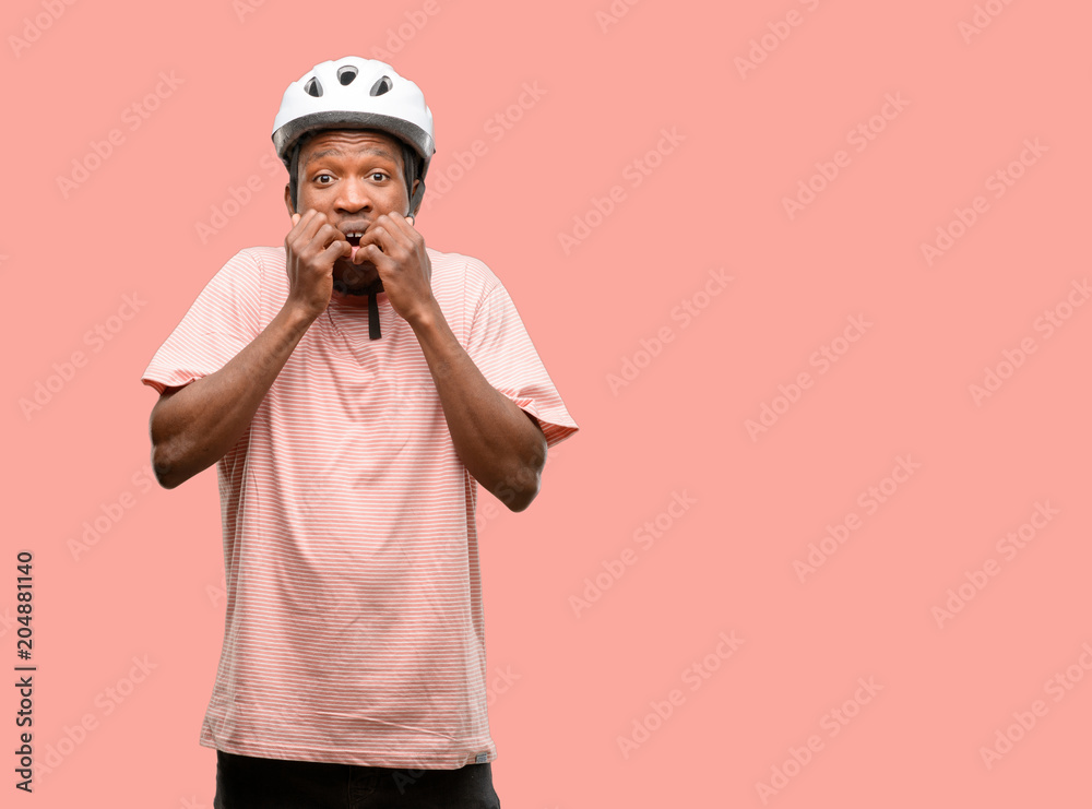 Black man wearing bike helmet terrified and nervous expressing anxiety and panic gesture, overwhelmed