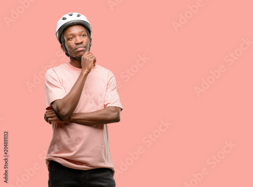 Black man wearing bike helmet thinking and looking up expressing doubt and wonder