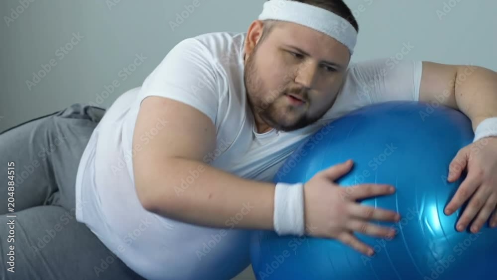 Exhausted fat man falling down on floor with fitness ball, lack of sport energy Exhausted fat man falling down on floor with fitness ball, lack of sport energy