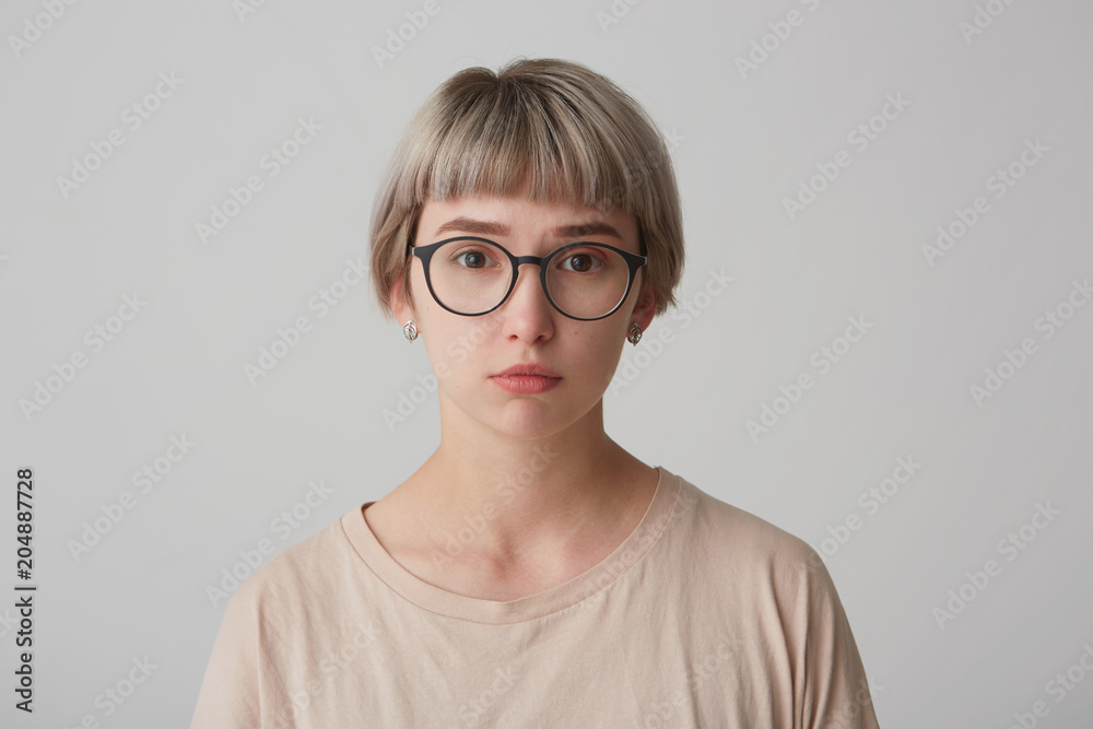 Serious female student, wears round spectacles and t shirt, looks self assured, sad and tired. Isolated over white background. Serious female student, wears round spectacles and t shirt, looks self assured, sad and tired. Isolated over white background.