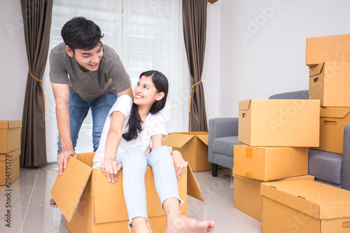 Happy asian couple is playing together with cardboard boxes in new house at moving day. photo