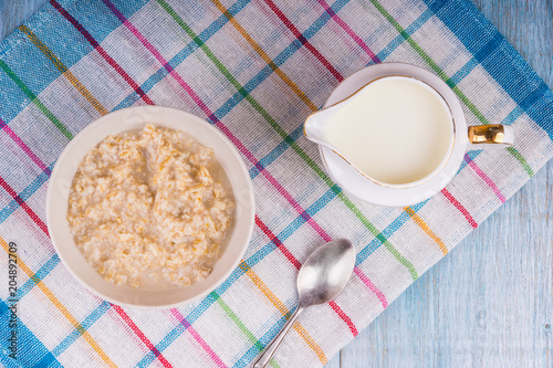 A cup of oatmeal and a jug of milk on a rustic napkin, top view - concept of dietary nutrition
