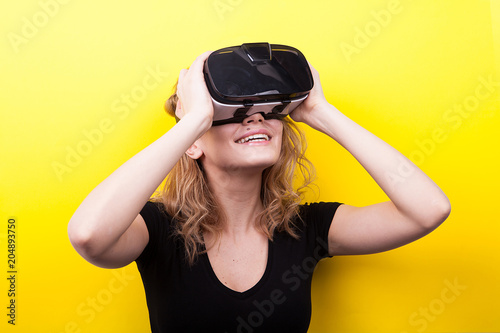Smilnig woman with a VR headset on enjoying virtual reality experience on yellow background in studio photo