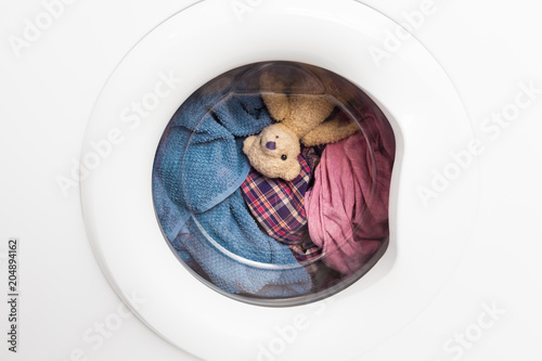 Wild Carousel Ride / Window door of washing machine with laundry and toy teddy bear inside who takes a look out (copy space)