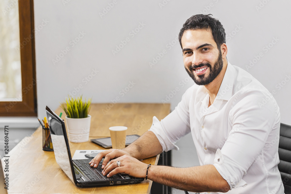 Dark-haired man in smart white shirt typing on laptop, concept of working atmosphere in the office Dark-haired man in smart white shirt typing on laptop, concept of working atmosphere in the office