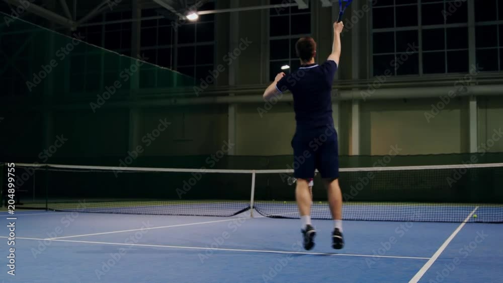 Serve by professional tennis player. Tennis serve indoor of tenis hall. Man on serve with tenis racket and dressed in black t-shirt, black shorts and black shoes.