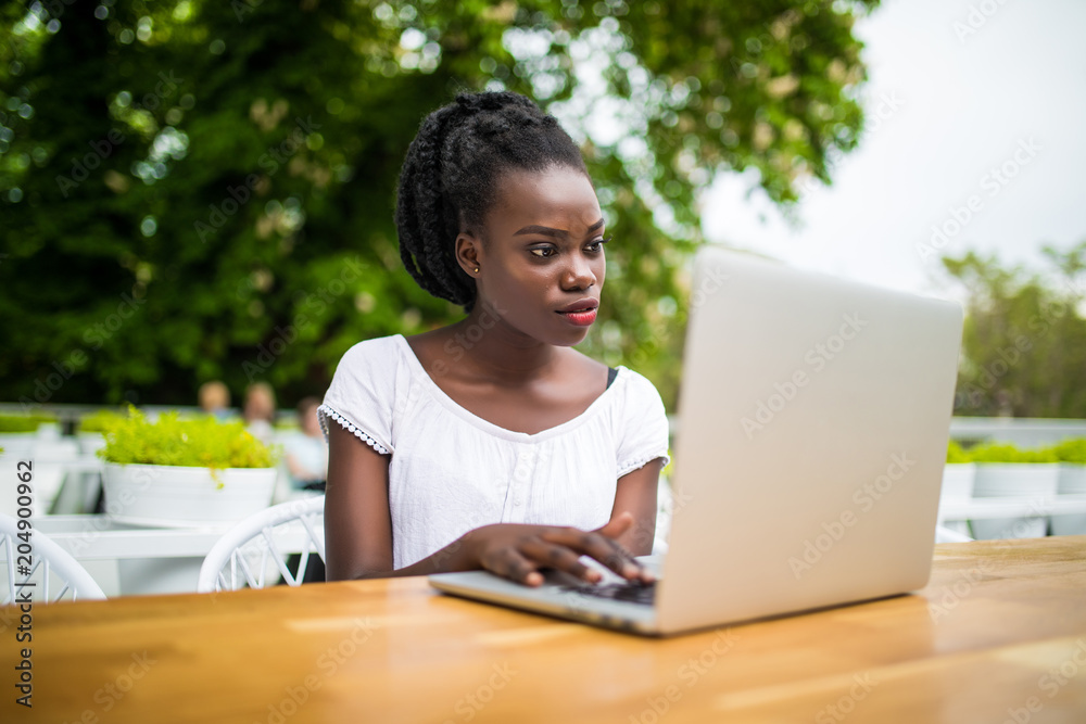 Afro american young black curly female is sitting in cafe and having remote work using laptop Afro american young black curly female is sitting in cafe and having remote work using laptop