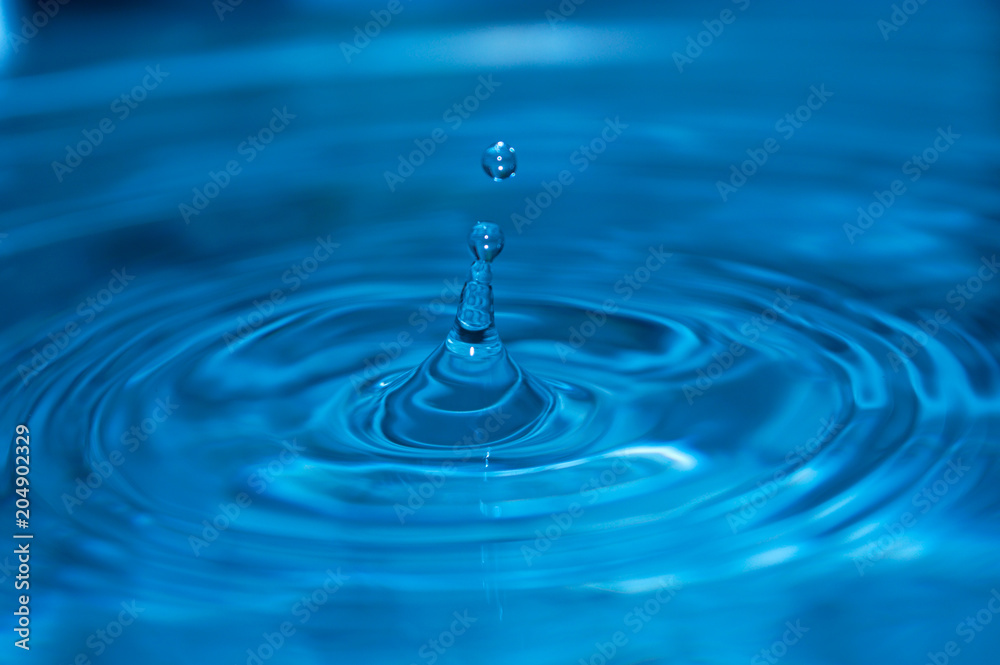 A drop of water falls in a blue water. A drop of water falls in a blue water.