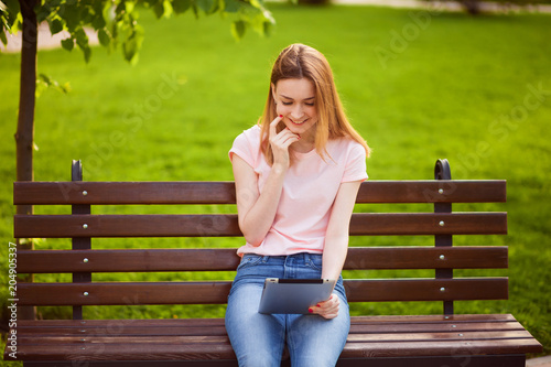 Girl with tablet sitting on a bench in the Park