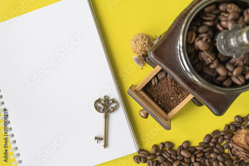 top view flat layer coofee hipster life stlye set, coffee beans, grinded beans in vintage wooden coffee grinder, blank book  and vintage key on yellow modern background photo