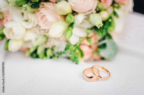 Wedding rings lie on white surface against background of bouquet of flowers