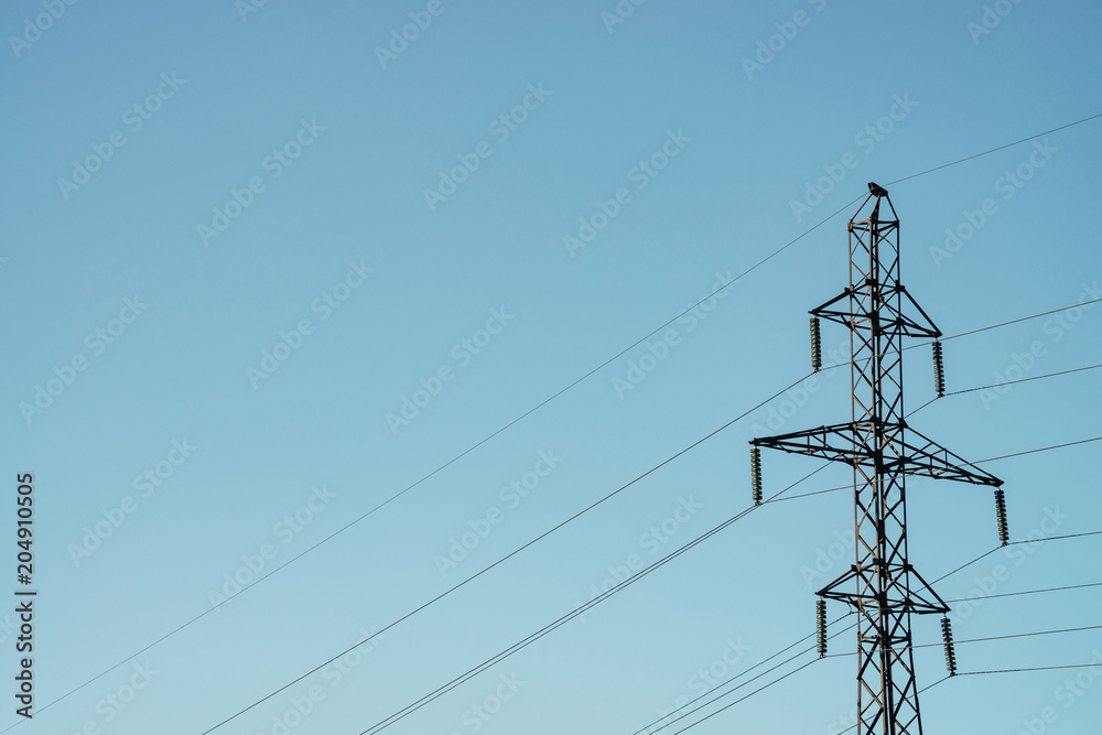 Posts with wires of high voltage on background of blue sky in sunlight. Background image of many wires in sky with copy space. Group of power lines.