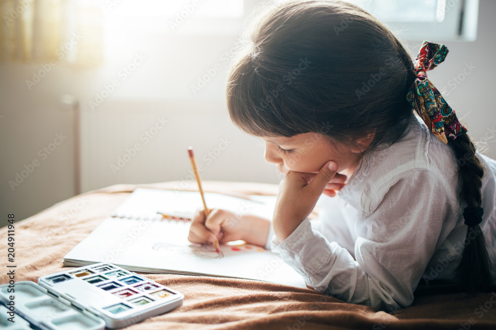 Beautiful little girl lying on the bed and drawing with pencils in color. Beautiful little girl lying on the bed and drawing with pencils in color.