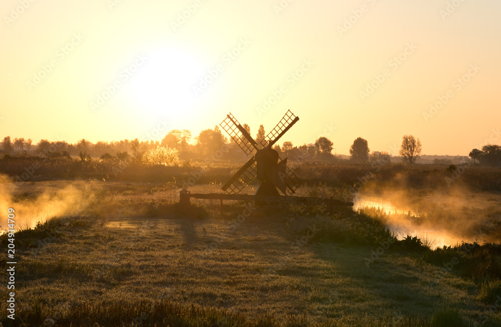 Fototapeta premium Fog at the river around a Dutch windmill at sunrise, Zaanse Schans, The Netherlands