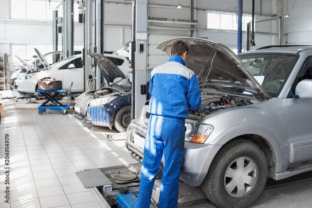 A mechanic working in a car workshop in a blue working form is repairing a gray car. Auto service.