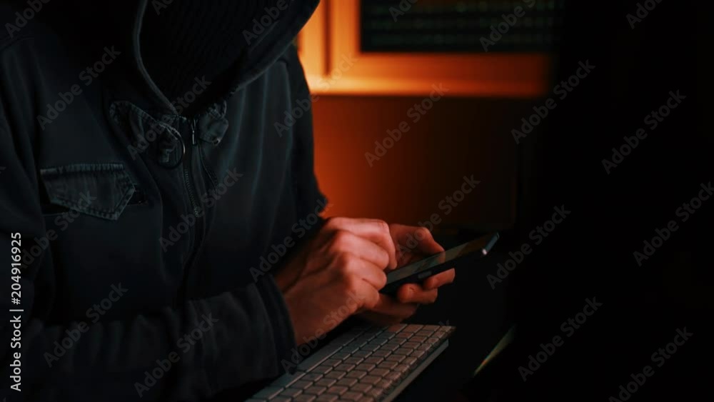 Computer hacker using smartphone device in dark interior, low key footage