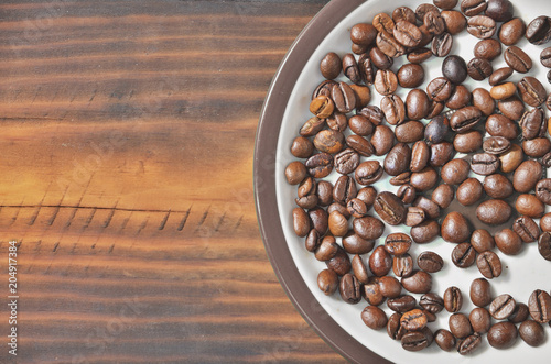 A saucer with coffee beans is on a wooden bed. photo