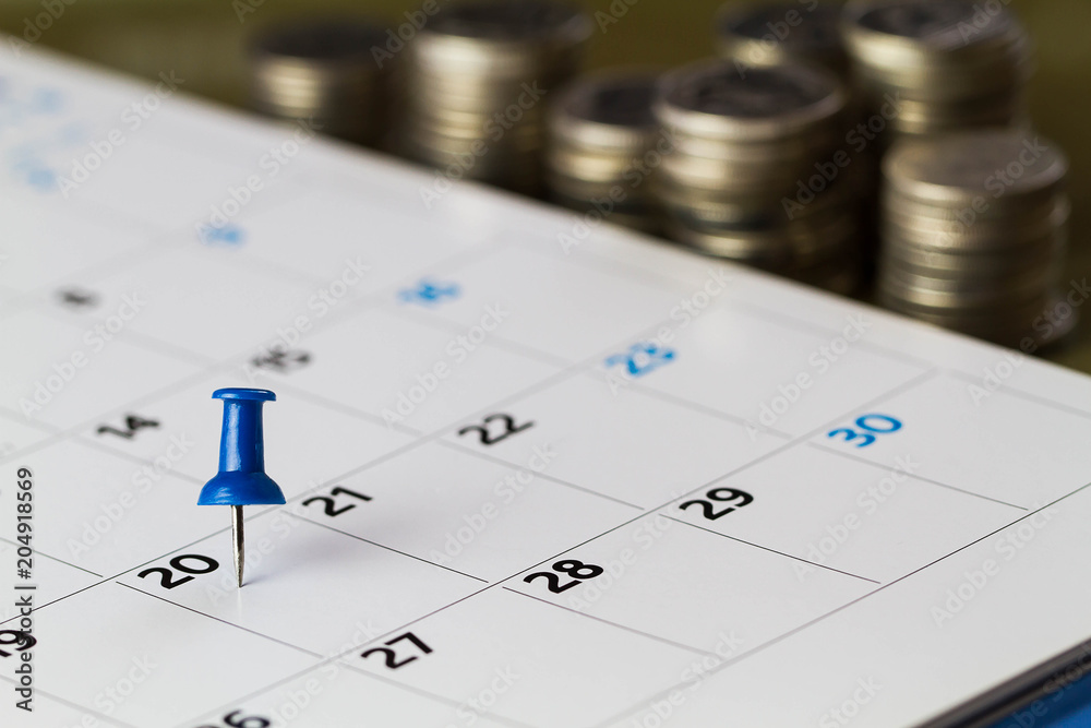 Pin on calendar on 20th of the month with blurred coins, business concept Pin on calendar on 20th of the month with blurred coins, business concept