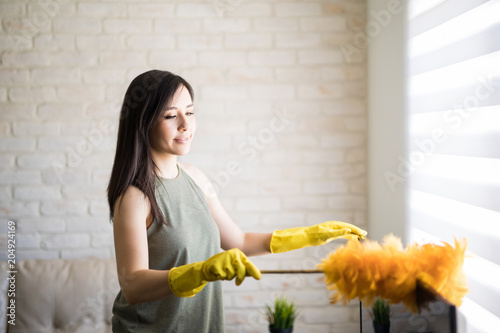Beautiful housewife using feather duster and cleaning her house