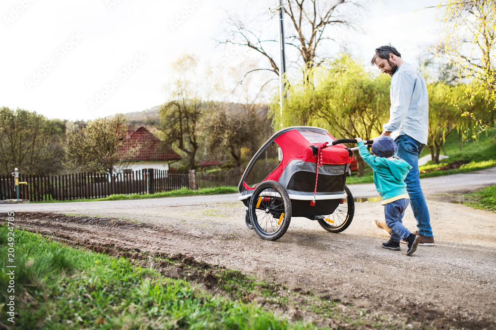A father with toddler son pushing a jogging stroller outside in spring nature. A father with toddler son pushing a jogging stroller outside in spring nature.
