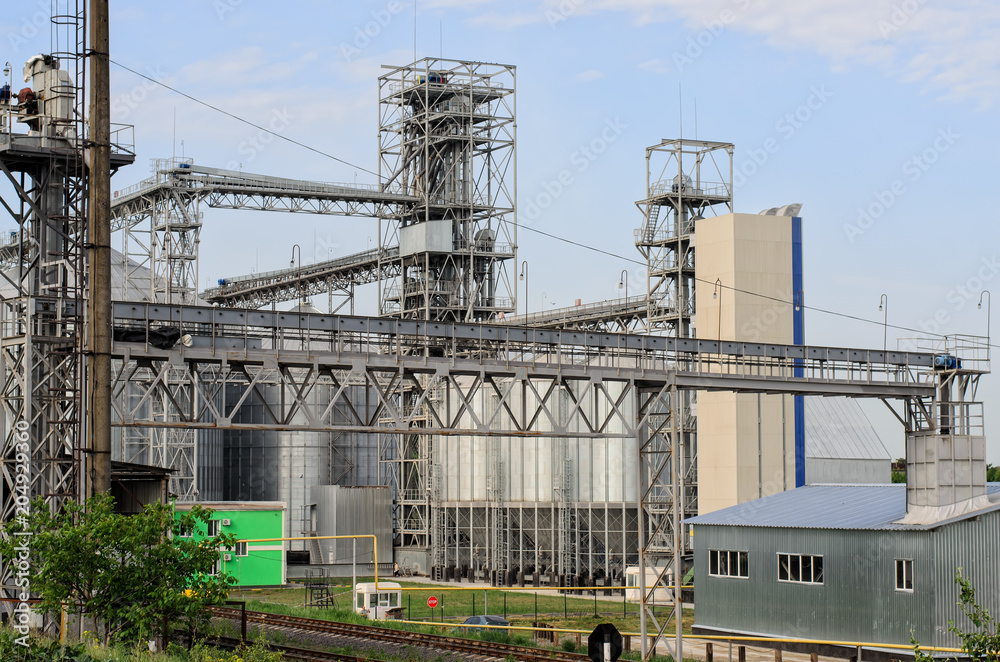 Part of modern working sugar plant (sugar refinery, factory), special metal equipment around, large metal tanks in the background, blue sky