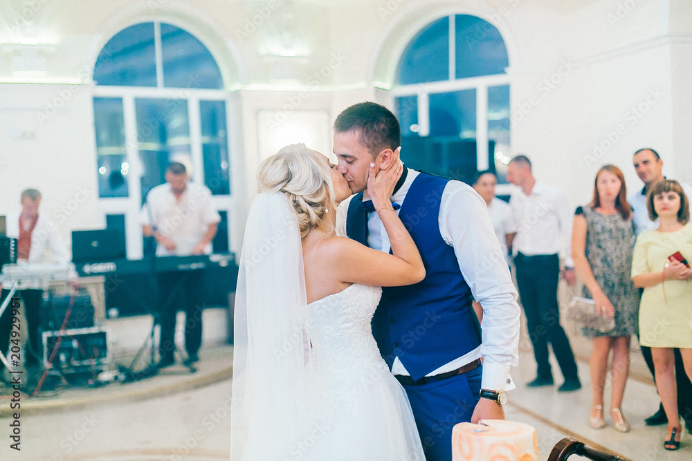 Naklejka premium Newlyweds cutting their delicious wedding cake. Wedding restaurant reception hall. Bride and groom stay near they wedding cake in peach color.