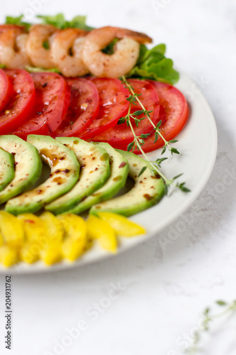 Avocado salad on a white background. Avocado, tomato, pepper and shrimps on a plate lined with rows