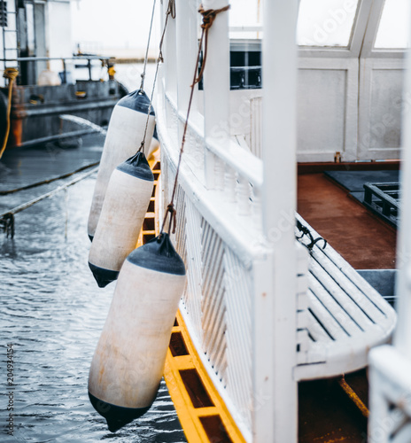 Vertical side view of a wooden boat for an underwater diving with multiple buoys on it; the wooden fisher nautical vessel with a yellow edging and a white body with hanging buffer buoys photo