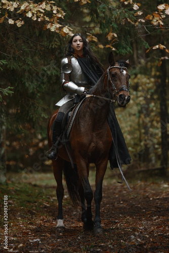 A beautiful warrior girl with a sword wearing chainmail and armor riding a horse in a mysterious forest.