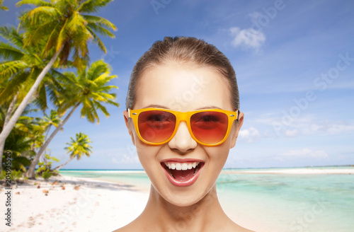 travel, tourism, summer holidays, vacation and people concept - smiling young woman or teenage girl in sunglasses over exotic tropical beach background