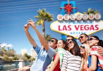 travel and tourism concept - group of happy friends taking selfie by cell phone over welcome to fabulous las vegas sign background