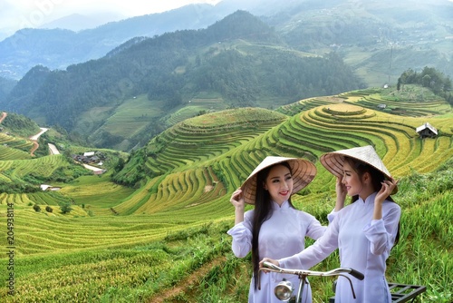 Two beautiful women with Vietnamese cultural dress, Ao dai and holding lotus flowers on rice fields on Mu Cang Chai, YenBai, rice fields prepare for harvest at Northwest Vietnam. photo