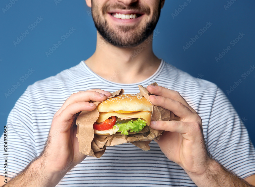 Man with yummy burger against color background