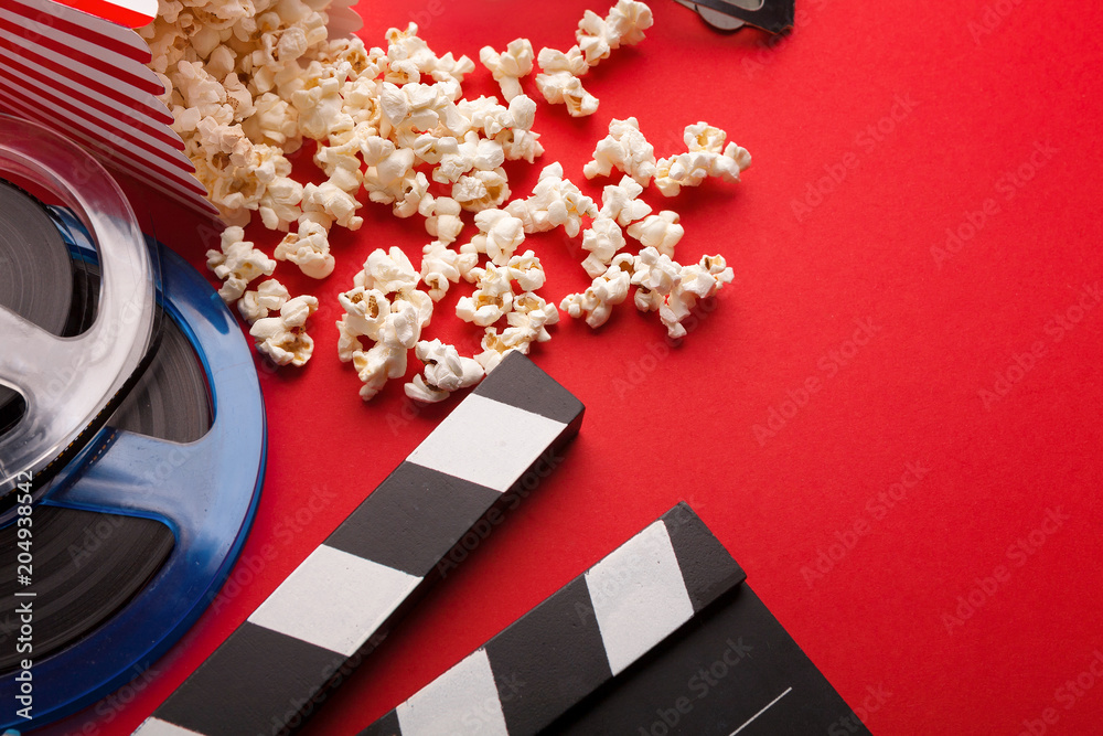 Clapperboard, film reel and popcorn on red background
