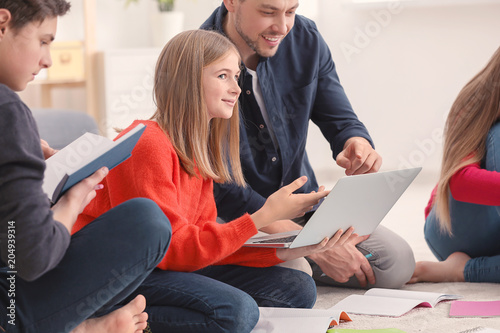 Group of teenagers doing homework with teacher indoors