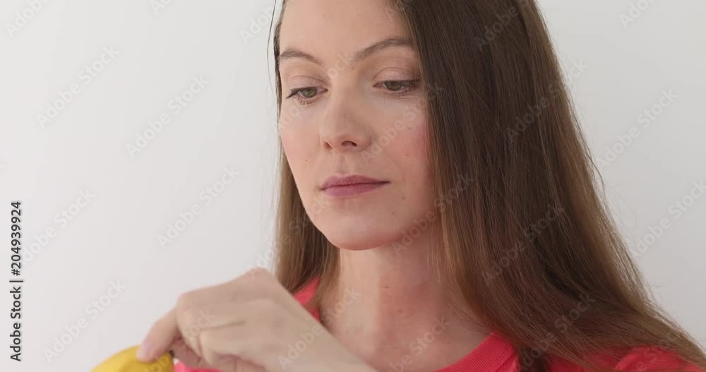 Seductive fair haired young woman peeling a banana and eating it white background. Girl looking at camera Seductive fair haired young woman peeling a banana and eating it white background. Girl looking at camera