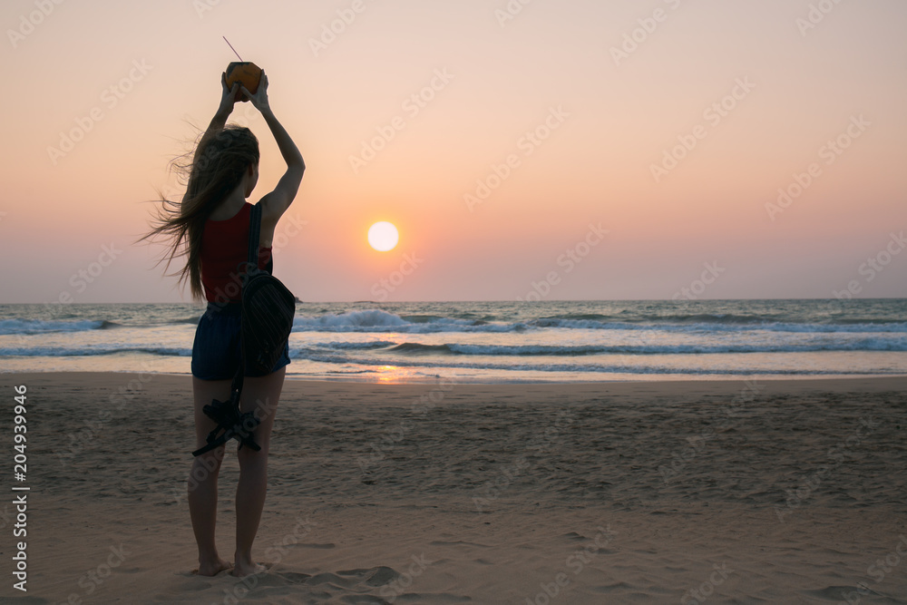 A woman with a coconut looks at the sunset