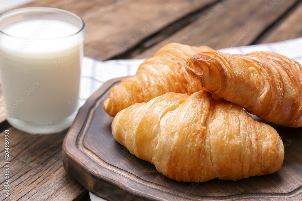 Wooden board with tasty croissants and glass of milk on table Wooden board with tasty croissants and glass of milk on table